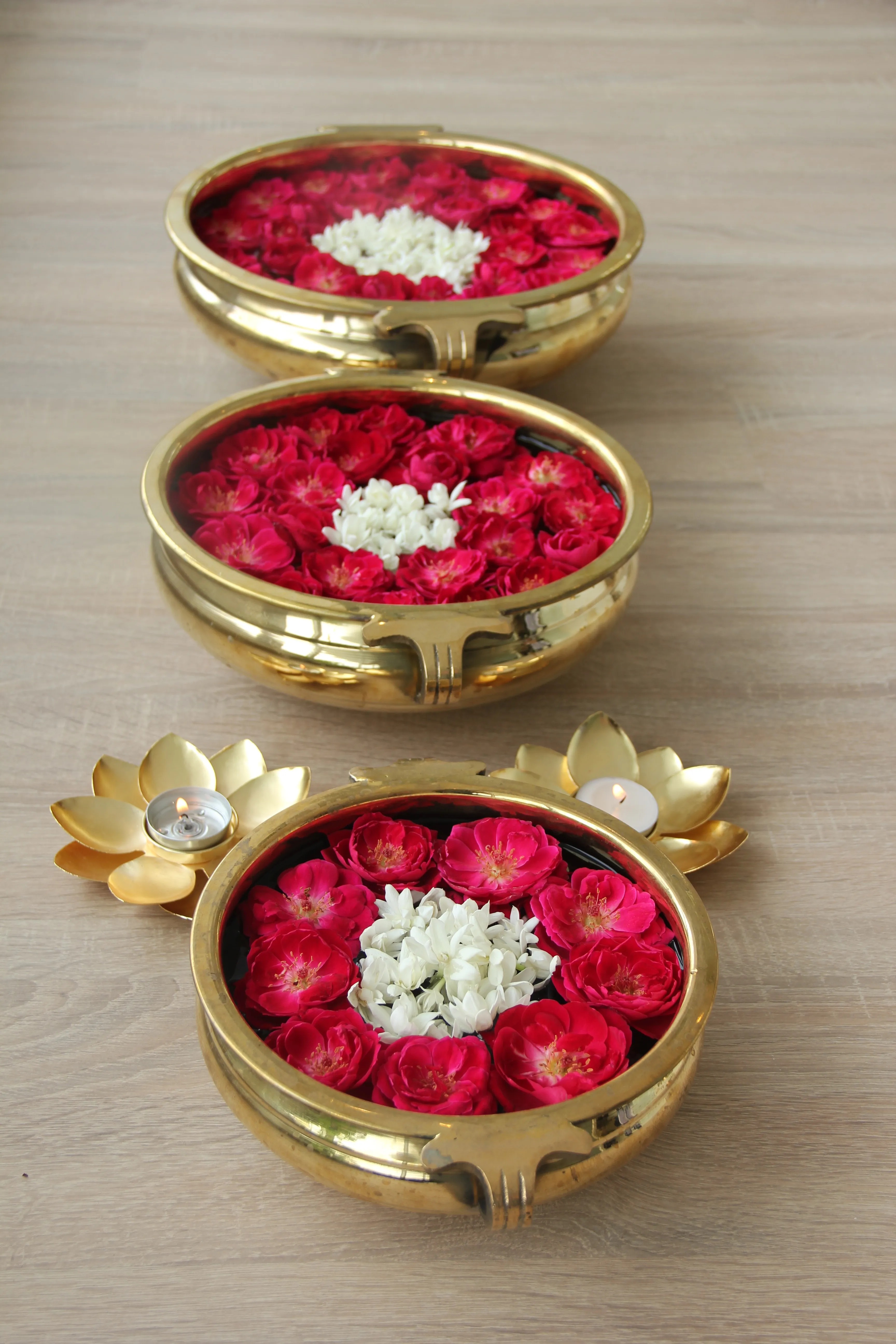 Brass bowls filled with rose and jasmine flowers beside lotus-shaped candle holders